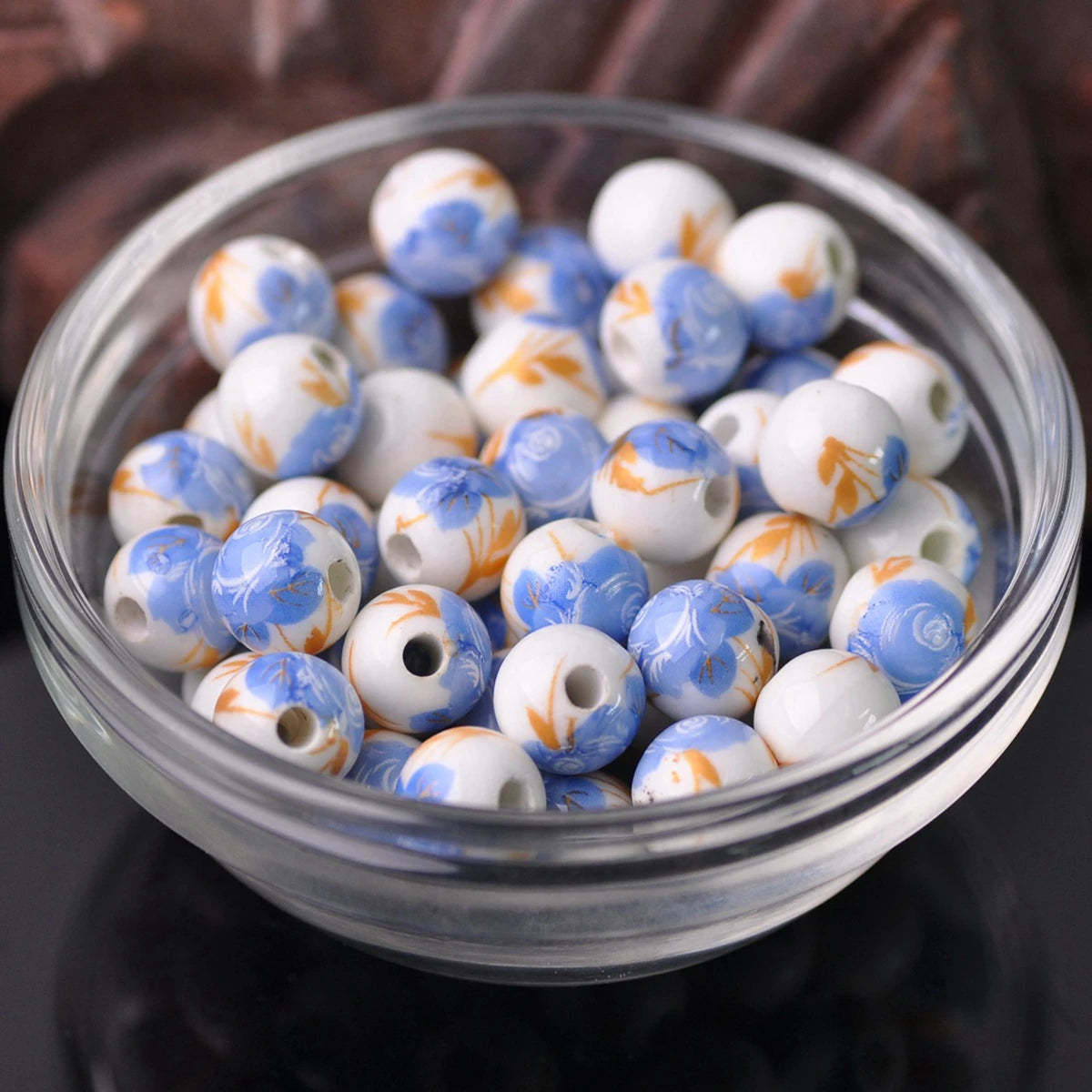 A clear glass bowl filled with small ceramic beads featuring blue and white floral patterns.