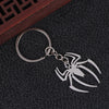 Silver pendant keychain charm shaped like a stylized spider on a dark surface.