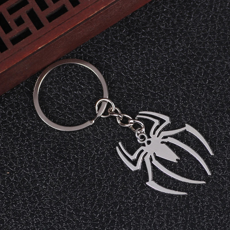 Silver pendant keychain charm shaped like a stylized spider on a dark surface.