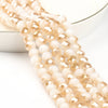 A strand of faceted crystal glass beads in a pale amber or champagne color, laid out on a white surface.