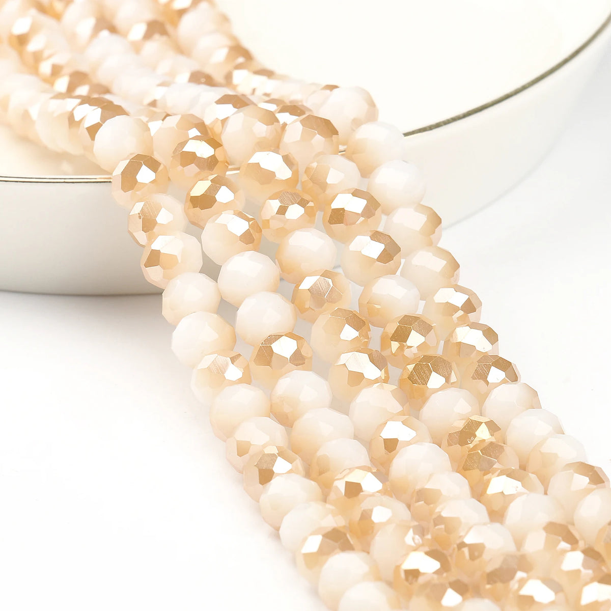 A strand of faceted crystal glass beads in a pale amber or champagne color, laid out on a white surface.