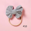 A gray knitted bow headband with a soft elastic band is displayed on a pink background.