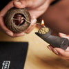 A hand holds a hemp wick with natural beeswax coating, lit and ready for use.