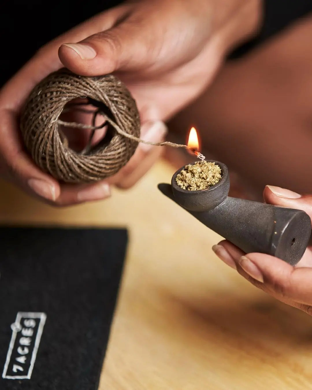 A hand holds a hemp wick with natural beeswax coating, lit and ready for use.