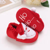 A pair of red baby winter boots with white trim and text on the toe featuring a festive design.