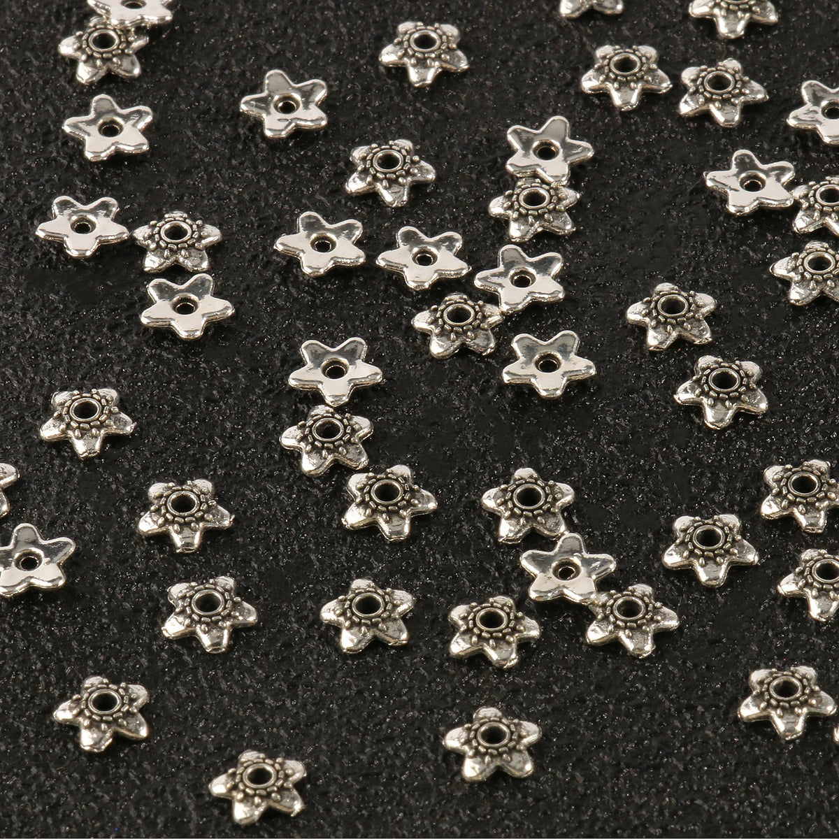 Small silver hollow flower bead caps scattered on a dark surface for jewelry making