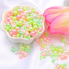 A bowl of assorted pink and green pearl beads next to a vibrant pink lotus flower.