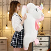 A young girl is holding a large white unicorn plush toy with pink accents in a brightly lit room.