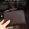 A dark brown genuine leather coin purse with a stitched flap and zipper is held in a hand on a wooden surface.