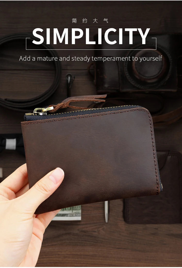 A dark brown genuine leather coin purse with a stitched flap and zipper is held in a hand on a wooden surface.