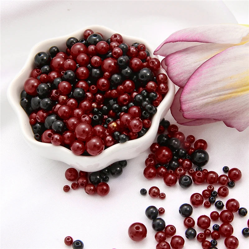A pile of assorted red and black pearl beads for jewelry making displayed on a white dish.