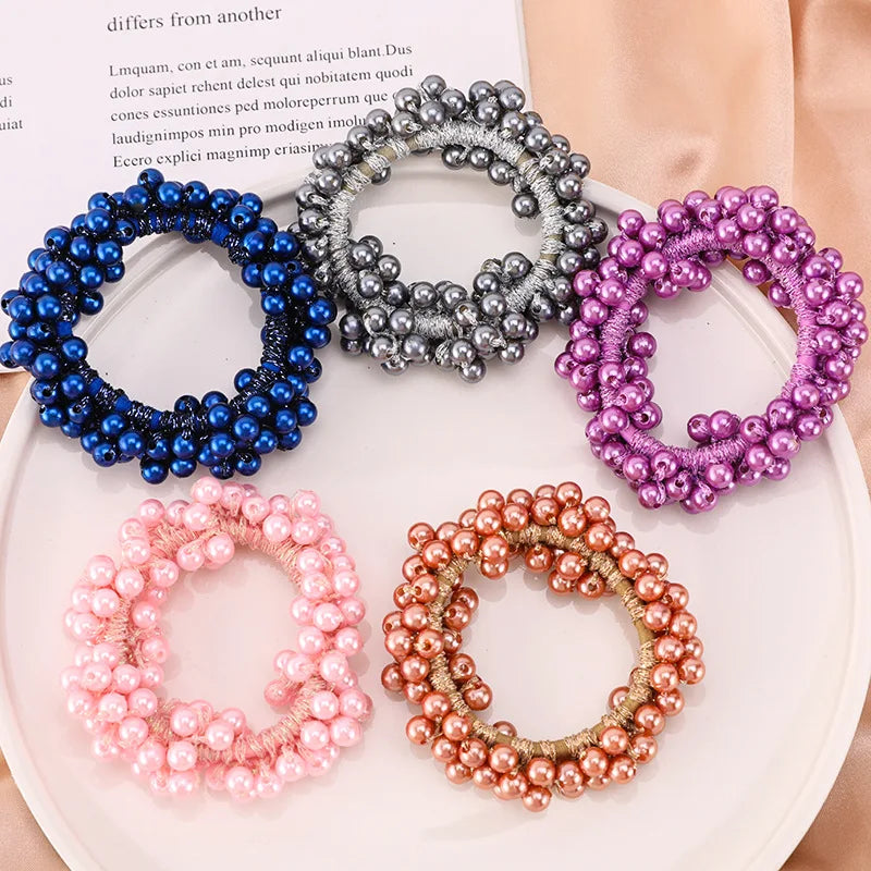 A collection of elegant pearl hair ties and bow scrunchies in various shades including blue, silver, purple, and pink.