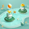 A green frog bath toy with a yellow head and other aquatic toys floating in light blue water.