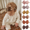 A close-up of a baby wearing a beige knitted outfit and a matching bow headband