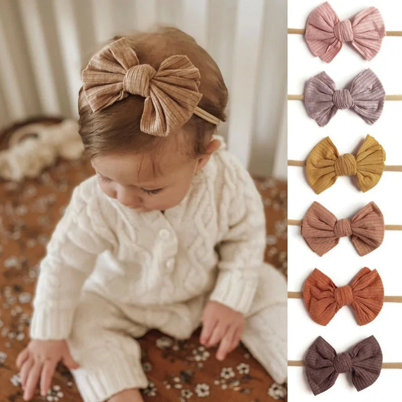 A close-up of a baby wearing a beige knitted outfit and a matching bow headband