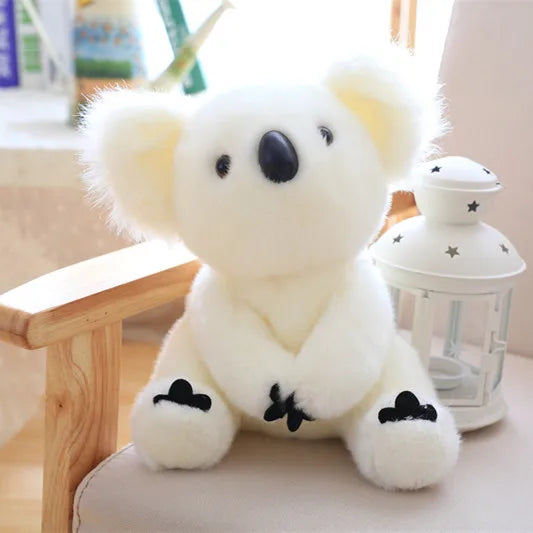 A white koala plush toy with black accents sitting on a wooden surface.
