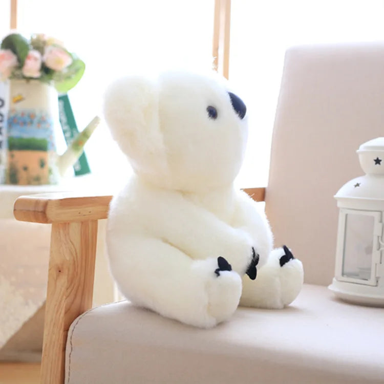 A white koala plush toy with black markings is resting on a light-colored surface next to a wooden stand.
