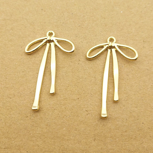 A pair of gold-colored alloy bow charms for jewelry making displayed on brown paper.