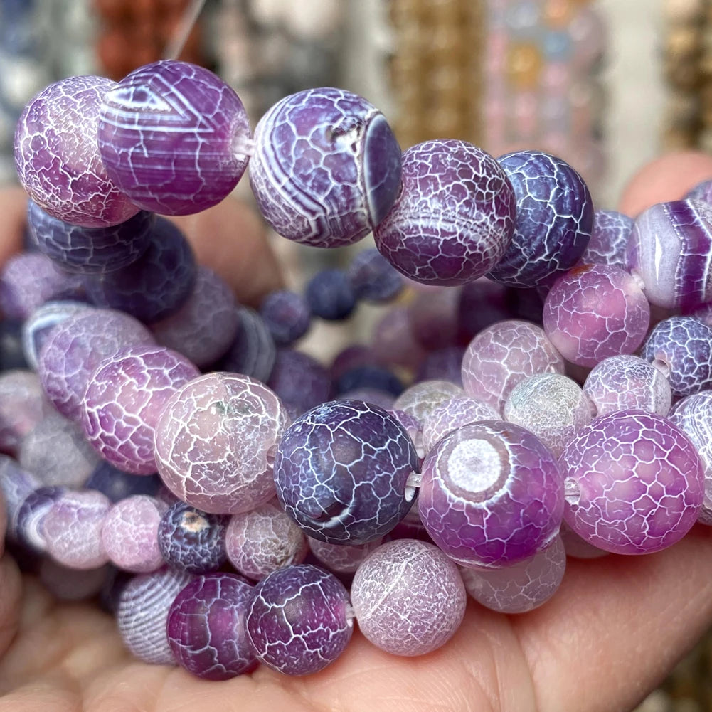 A hand holds a collection of polished natural gemstone beads in shades of purple and pink.