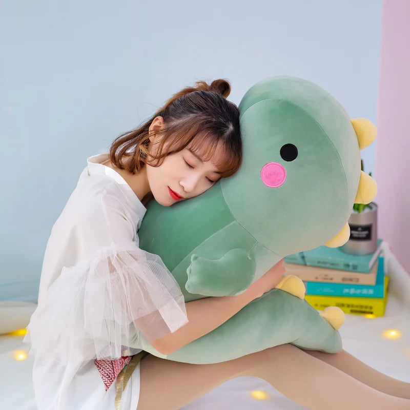 A woman is hugging a large, soft green dinosaur plush toy indoors.