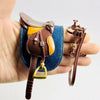 A brown leather horse saddle and riding prop accessory is held in a hand.
