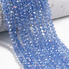 A close-up of blue faceted crystal glass beads strung together on a white surface.
