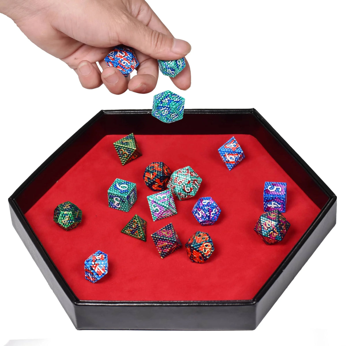 A hand holds several colorful hexagonal dice inside a black tray with a red velvet interior.