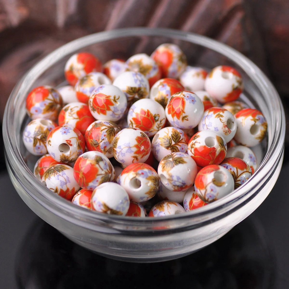 A clear glass bowl filled with small, round ceramic beads featuring a floral pattern in shades of orange, white, and purple.