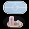 A clear silicone mold with measurement lines is shown above a small pink vase and a white patterned planter on a wooden tray.