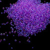 A pile of small, translucent purple glass bubble beads scattered against a black background.