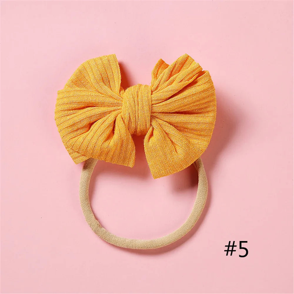 A bright orange, textured fabric bow headband with a light beige elastic band on a pink background.