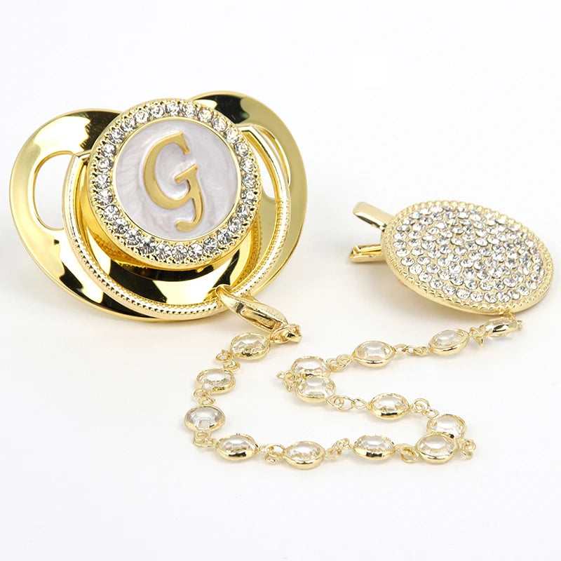 Gold rhinestone pacifier featuring a large initial G on a white background with a clip and chain.
