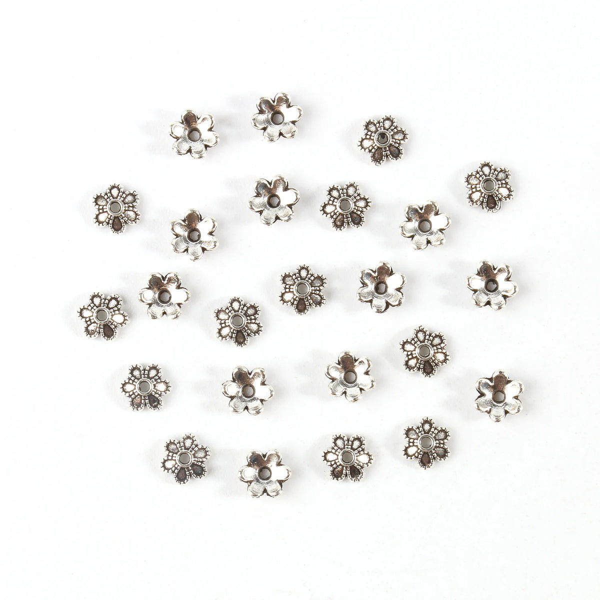 A collection of small, silver-toned Tibetan style hollow flower bead caps for jewelry making.