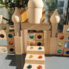 A stack of wooden building blocks shaped like pillars holds a dome-like piece, with various colored acrylic gemstones placed 