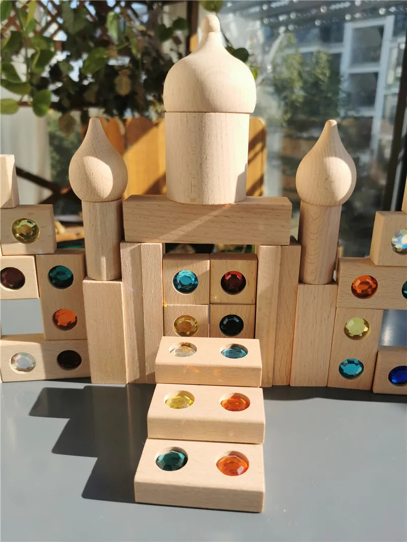 A stack of wooden building blocks shaped like pillars holds a dome-like piece, with various colored acrylic gemstones placed 