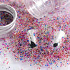 A close-up of iridescent mini glass bubble beads scattered on a white surface next to a clear plastic bottle.
