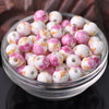 A clear glass bowl filled with pink and white floral ceramic beads for jewelry making