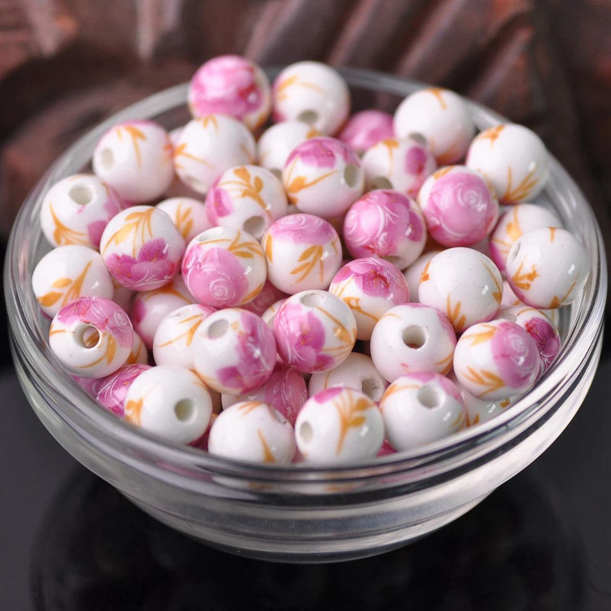 A clear glass bowl filled with pink and white floral ceramic beads for jewelry making