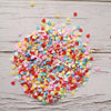 A pile of heart-shaped fake candy sprinkles in various colors like pink, yellow, and red scattered on a light wooden surface.