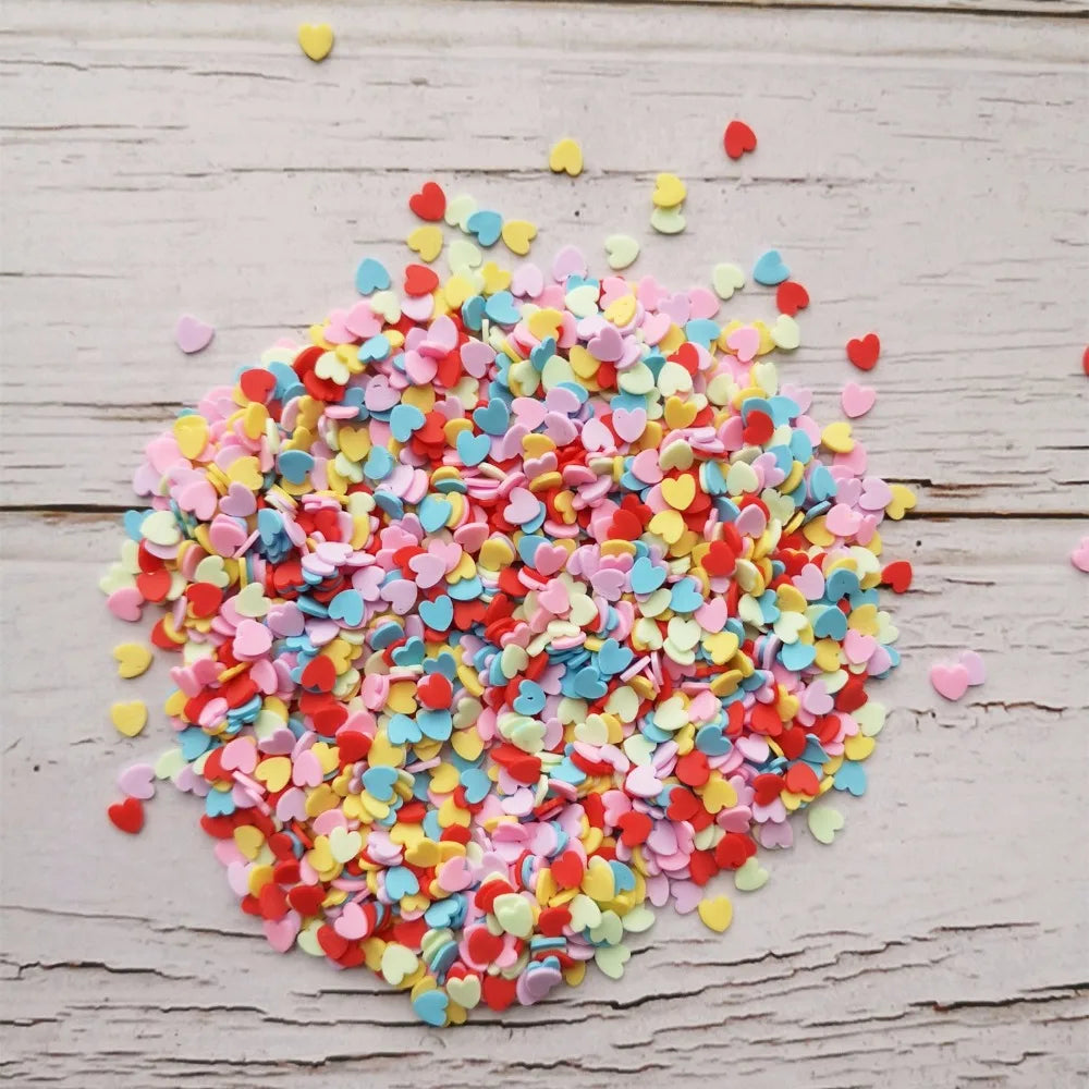 A pile of heart-shaped fake candy sprinkles in various colors like pink, yellow, and red scattered on a light wooden surface.