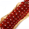 A wooden skewer holds a string of natural red carnelian round beads for jewelry making.