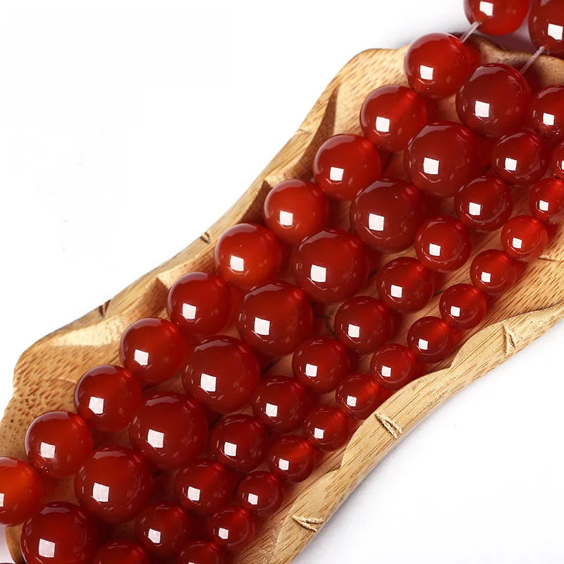 A wooden skewer holds a string of natural red carnelian round beads for jewelry making.
