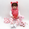A baby doll wearing a pink hooded jacket and matching pants sits next to a pink stuffed giraffe.