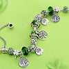 A silver charm bracelet featuring green crystal beads and floral accents, displayed on a light green background.