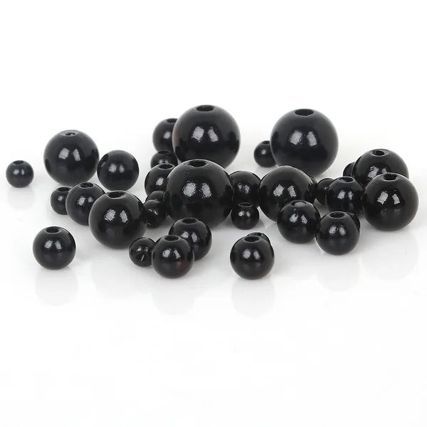 A collection of smooth, black imitation pearl beads scattered on a white surface.