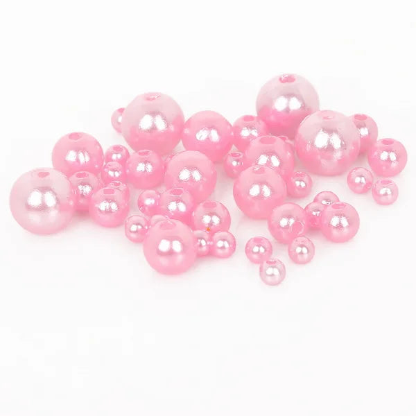A collection of pink and magenta imitation pearl beads scattered on a white background.