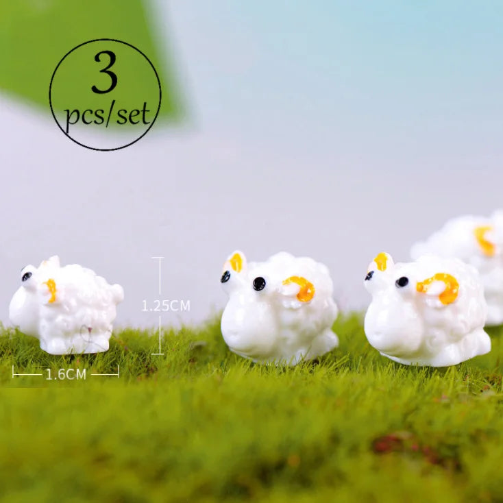 Three white fluffy animal figurines with yellow accents displayed on green grass.