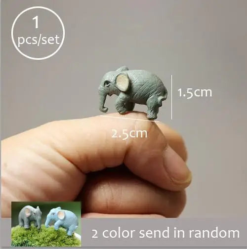 A hand holds a small gray elephant figurine, demonstrating the size of the miniature animal for fairy gardens.