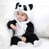 A baby wearing a black and white animal hooded romper sitting on a white couch.