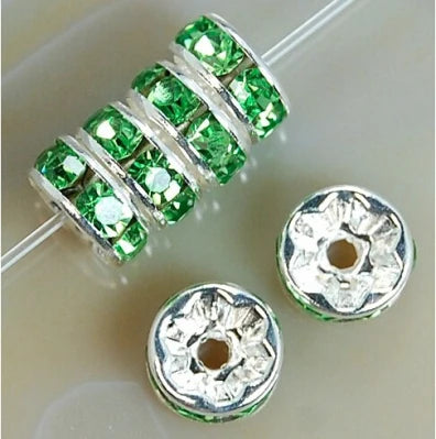 A string of green crystal rondelle spacer beads is shown next to two individual beads on a white background.